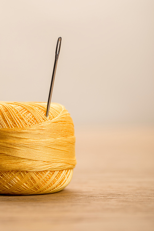 selective focus of yellow cotton knitting yarn ball with needle isolated on beige with copy space