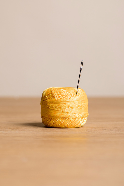 selective focus of yellow cotton knitting yarn ball with needle isolated on beige