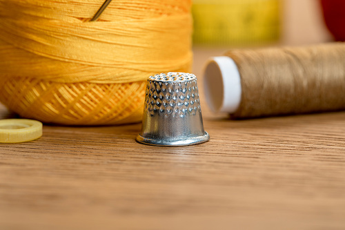 close up view of thimble with yarn ball and thread coil on wooden table
