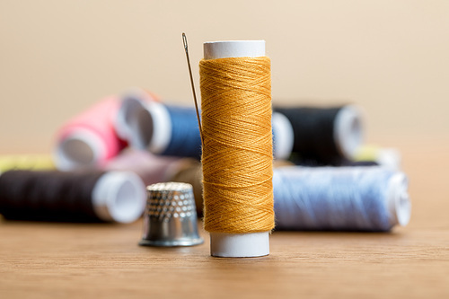 selective focus of cotton thread coil with needle isolated on beige