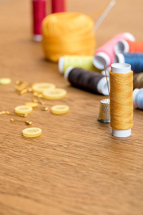 selective focus of thimble and yellow thread coil with needle on wooden table with copy space