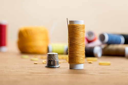 selective focus of thread coil with thimble on wooden table isolated on beige