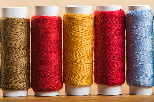 close up view of colorful cotton thread coils in row isolated on beige