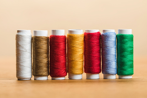colorful cotton thread coils in row on wooden table isolated on beige
