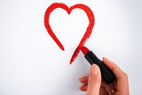 cropped view of woman drawing heart while holding red lipstick isolated on white