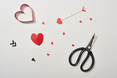 Top view of heart shaped papers with arrows and scissors on grey background