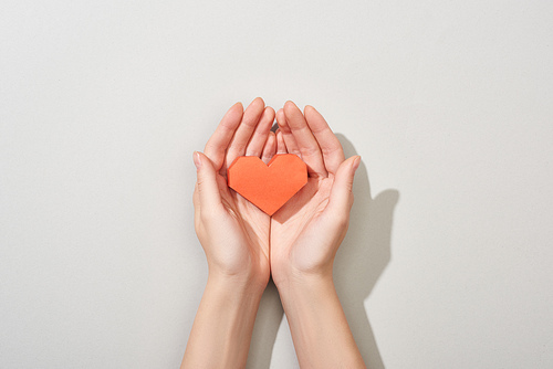 Top view of girl holding paper heart in hands on grey background, cropped view