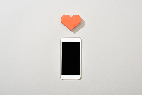 Top view of smartphone with blank screen and paper heart on grey background