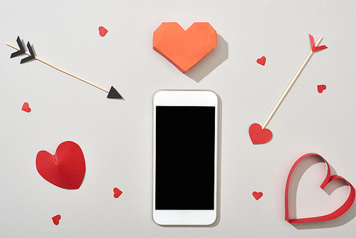 Top view of smartphone with blank screen and heart shaped papers with arrows on grey background