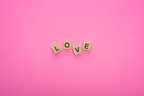 top view of love lettering on wooden cubes on pink background