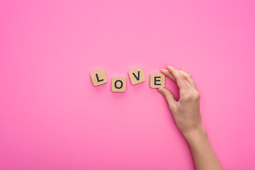 partial view of woman holding cubes with love lettering on pink background