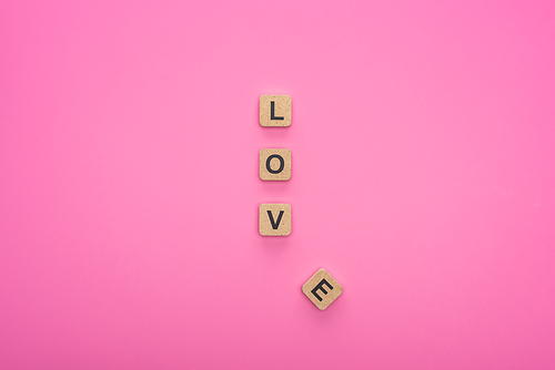 top view of love lettering on wooden cubes isolated on pink background