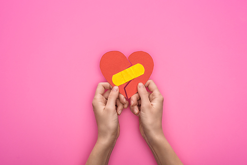 cropped view of holding broken paper heart with patch isolated on pink background