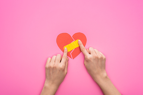 cropped view of woman putting patch on broken paper heart isolated on pink background