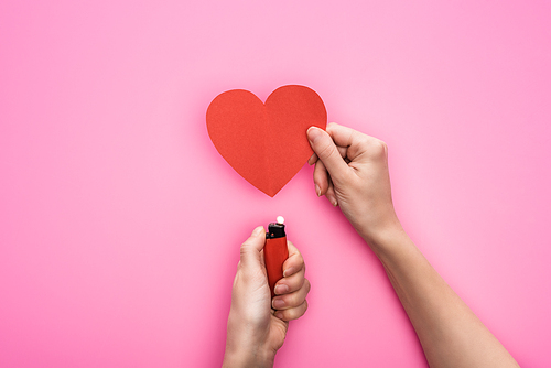 cropped view of woman lighting up empty red paper heart with lighter isolated on pink