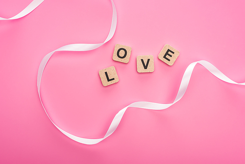 top view of curved ribbon and wooden blocks with love lettering isolated on pink