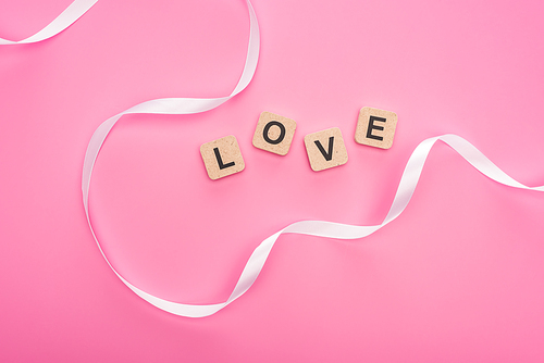 top view of curved ribbon and wooden blocks with love lettering isolated on pink
