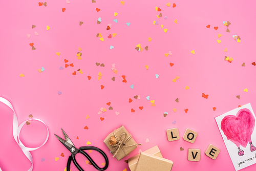 top view of valentines confetti, empty compact disk, scissors, gift boxes, greeting card and cubes with love lettering on pink background