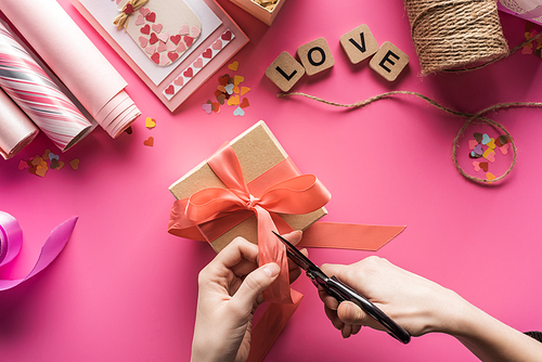 cropped view of woman cutting ribbon while making valentines gift on pink background