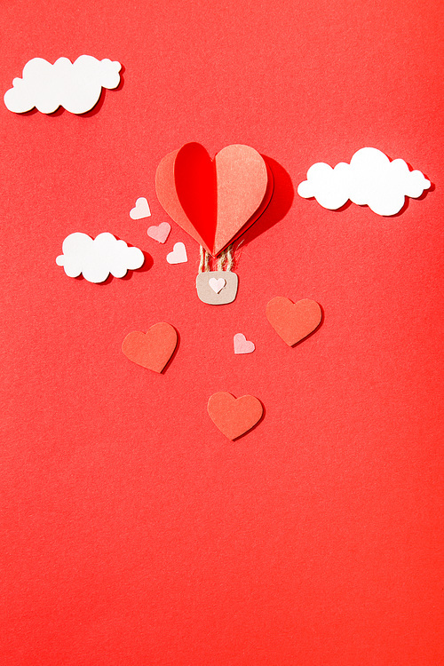 top view of paper heart shaped air balloon in clouds on red background