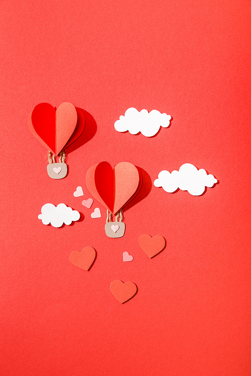 top view of paper heart shaped air balloons in clouds on red background
