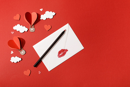 top view of paper clouds and heart shaped air balloons, envelope with lip  and pencil on red background