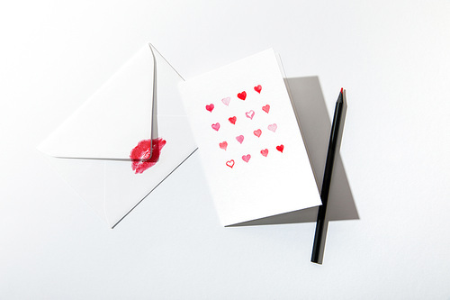 top view of greeting card with hearts near envelope with lip  and pencil on white background