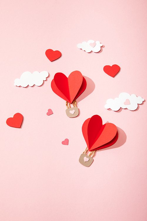 top view of paper heart shaped air balloons in clouds on pink