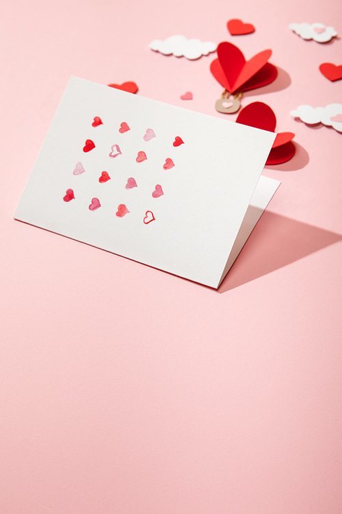 selective focus of greeting card with hearts near paper heart shaped air balloons in clouds on pink