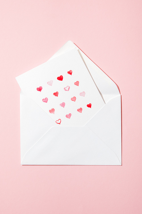top view of greeting card with hearts in white envelope isolated on pink