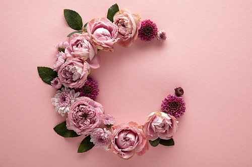 top view of blooming spring flowers arranged as letter C on pink background