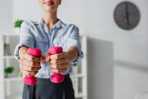 cropped view of businesswoman training with pink dumbbells in office