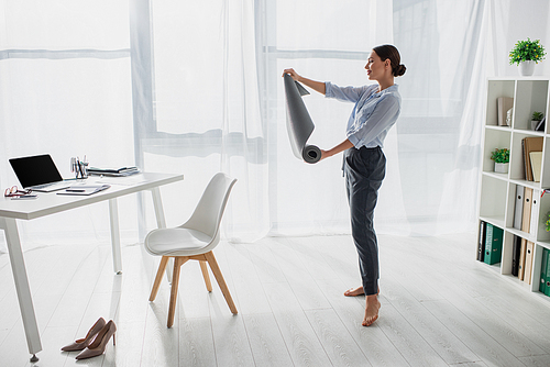 beautiful young businesswoman holding yoga mat in office