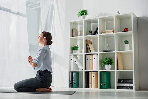 businesswoman practicing yoga and meditating with namaste gesture on mat in office