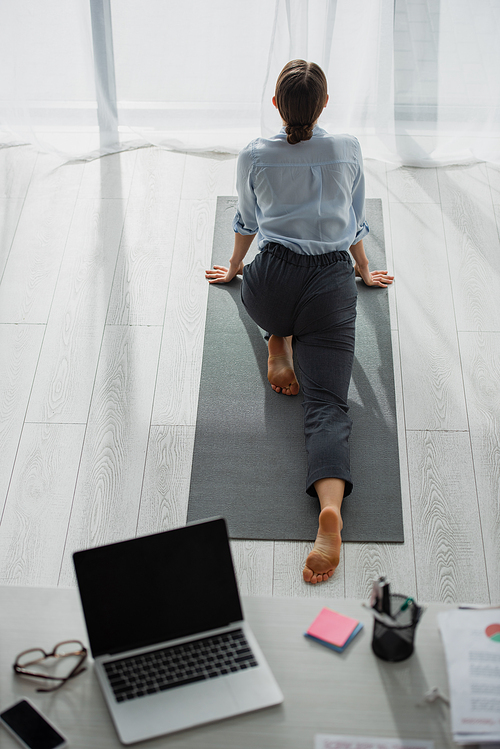 back view of businesswoman practicing yoga and stretching legs on mat in office