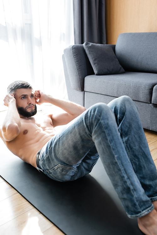 Handsome shirtless man doing abs on fitness mat in living room