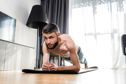 Surface level of shirtless man doing plank on fitness mat at home