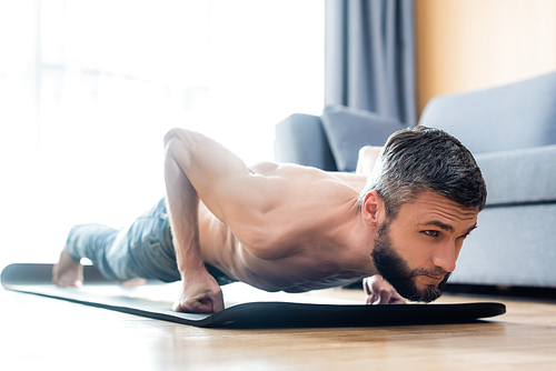 Surface level of handsome shirtless man doing press ups while exercising on fitness mat at home