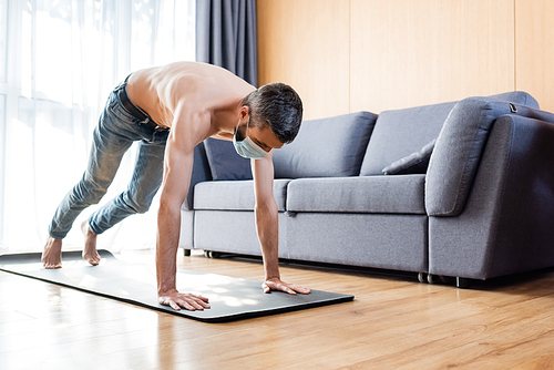 Shirtless man in medical mask working out on fitness mat at home