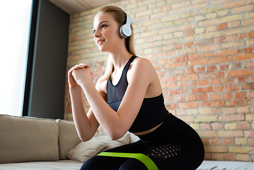 happy sportswoman in wireless headphones doing squat exercise at home