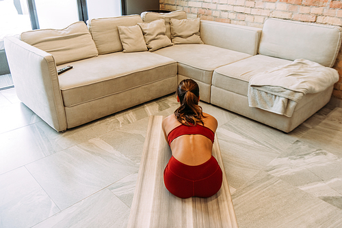 Back view of girl stretching on yoga mat at home on self isolation