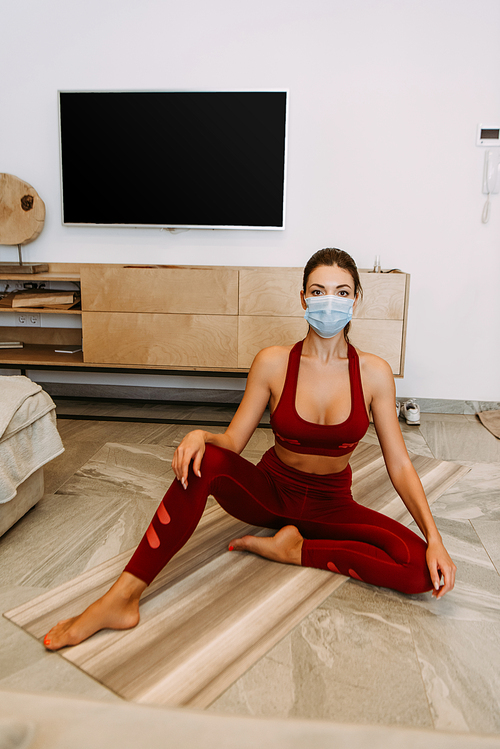girl in medical mask practicing yoga on mat at home on self isolation