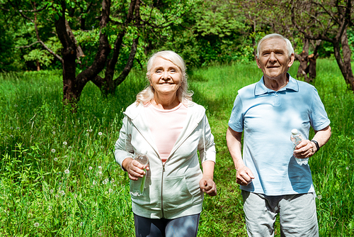 cheerful woman and man with grey hair running in park