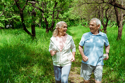 cheerful woman with grey hair looking at husband while running in park