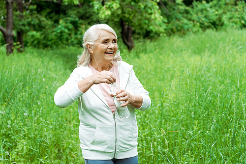 cheerful senior woman with grey hair holding bottle with water