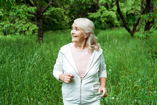 happy senior woman with grey hair running in green park