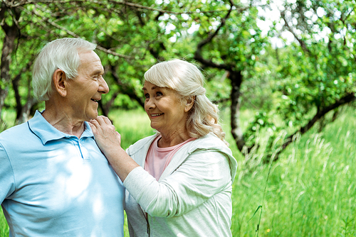 cheerful retired man looking at happy wife in green park