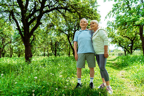 low angle view of cheerful senior man standing with wife in green park