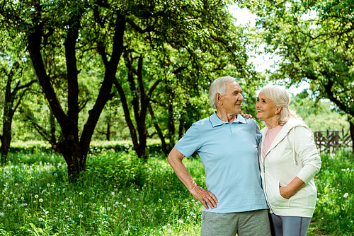 cheerful senior man standing with hand on hip near wife with hand in pocket