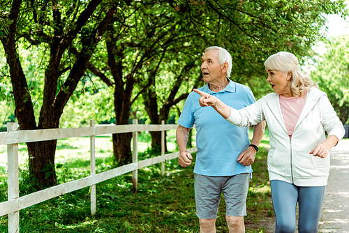 retired woman with grey hair pointing with finger near surprised husband